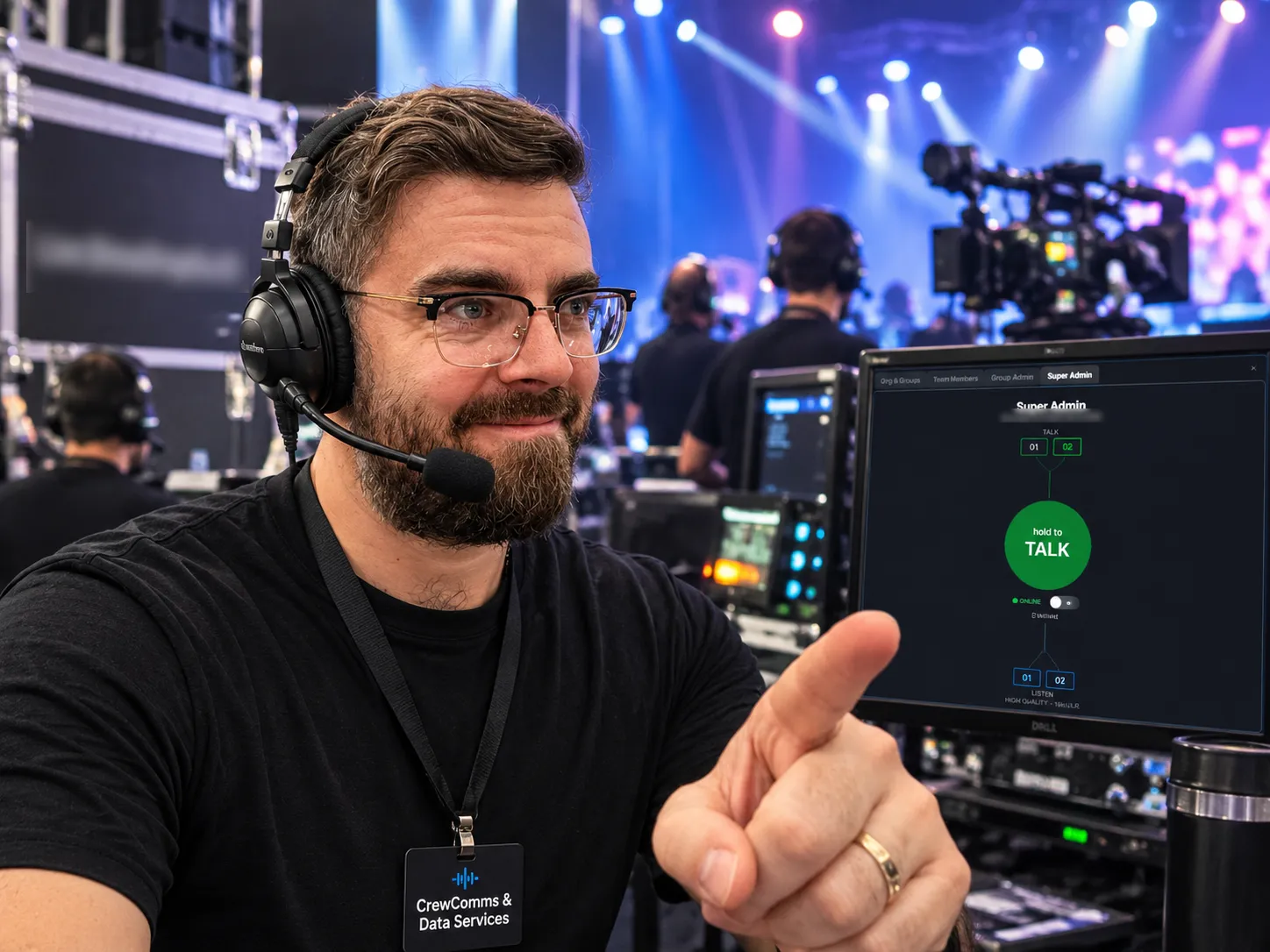 A crew member in a headset at a live event control desk, pointing to ShowDropGo Comms on a monitor